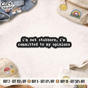 May include: A black embroidered patch with a white stitched border and the text "i'm not stubborn, i'm committed to my opinions" in a typewriter-style font. The patch has a rectangular shape with rounded, irregular edges.