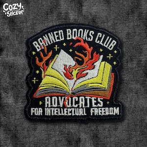 May include: Embroidered patch with the text "BANNED BOOKS CLUB" and "ADVOCATES FOR INTELLECTUAL FREEDOM". The patch features a burning book design with yellow, red, and white details, set against a black background.