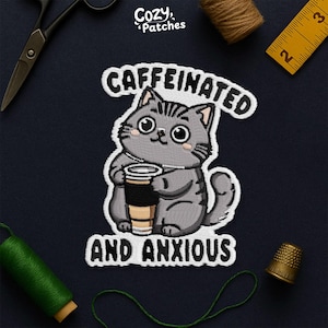 May include: Embroidered patch featuring a gray cartoon cat holding a coffee cup. The patch has the text "CAFFEINATED AND ANXIOUS" in white lettering. The patch is surrounded by sewing supplies, including scissors, thread, and a thimble.