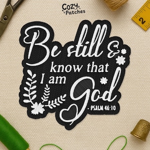 May include: Black embroidered patch with the words "Be still & know that I am God" in white script. The patch includes floral and heart accents, with "Psalm 46:10" at the bottom. The patch is surrounded by sewing tools.
