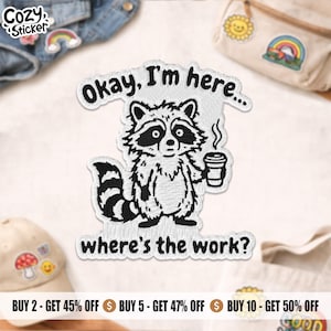 May include: A black and white embroidered patch depicting a raccoon with a coffee cup. The text on the patch reads "Okay, I'm here... where's the work?" The patch has a Cozy Sticker logo in the upper left corner.