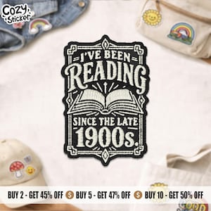 May include: A rectangular embroidered patch with a black background and white stitching. The design features an open book icon centred above the text I'VE BEEN READING SINCE THE LATE 1900s. The text is framed by a decorative border with ornate corners.