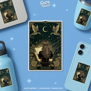 May include: A sticker featuring a tarot card design with a woman reading a book, framed by dragons and roses. The text "THE READER" is at the bottom. The sticker is on a laptop, phone, and water bottle.