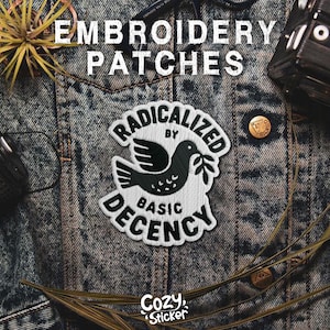 May include: Embroidered patch with a black and white dove design holding an olive branch, with the text "RADICALIZED BY BASIC DECENCY." The patch is on a denim jacket. The brand "Cozy Sticker" is also visible.