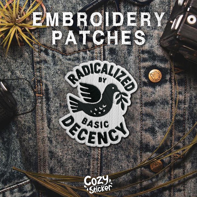 May include: Embroidered patch with a black and white dove design holding an olive branch, with the text "RADICALIZED BY BASIC DECENCY." The patch is on a denim jacket. The brand "Cozy Sticker" is also visible.