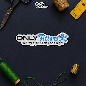 May include: Embroidered patch with the text "ONLY Fitters" in white and blue, featuring a wrench and pipe symbol. The phrase "We lay pipe all day and night" is below the main text. The patch is on a dark blue background.