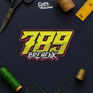 May include: Embroidered patch with the text "789 BREHENK" in yellow, red, and white. The patch is on a navy blue background, with sewing tools and thread visible.