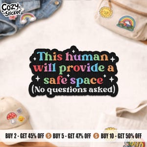 Peut inclure: Un écusson noir brodé avec le texte "This human will provide a safe space (No questions asked)" en lettres colorées. L'écusson a une bordure noire et de petites étoiles blanches. Le logo Cozy Sticker est en haut à gauche.