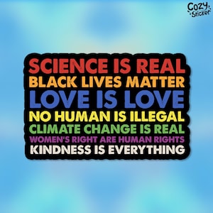 May include: A black and white sticker with rainbow colored text that reads "Science is real, Black Lives Matter, Love is Love, No Human is Illegal, Climate Change is Real, Women's Right are Human Rights, Kindness is Everything".