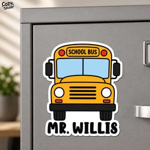 May include: A yellow school bus sticker with a white border, featuring a light blue windshield, black side mirrors, and a black bumper. The text SCHOOL BUS is printed in black on the top, and the name MR. WILLIS is printed in black below the bus.