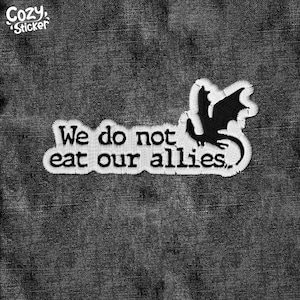 May include: White embroidered patch with the text "We do not eat our allies." and a black dragon silhouette. The patch is set against a dark grey denim background. The Cozy Sticker logo is in the upper left corner.