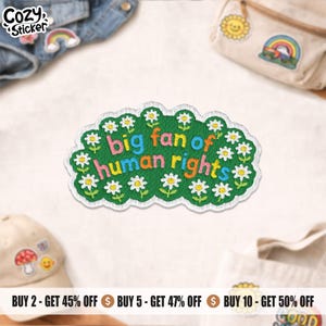 May include: An embroidered patch with the words "big fan of human rights" in colourful letters on a green background, framed by white daisies. The patch has a white border and is a decorative item.