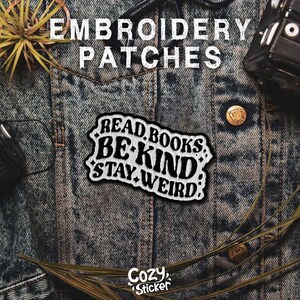 May include: White embroidered patch on a denim background. The patch says "Read Books Be Kind Stay Weird".