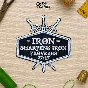 May include: A black and white embroidered patch with the text "IRON SHARPENS IRON PROVERBS 27:17" and three swords. The patch is in a shield shape with a white border. The brand name "Cozy Patches" is at the top.
