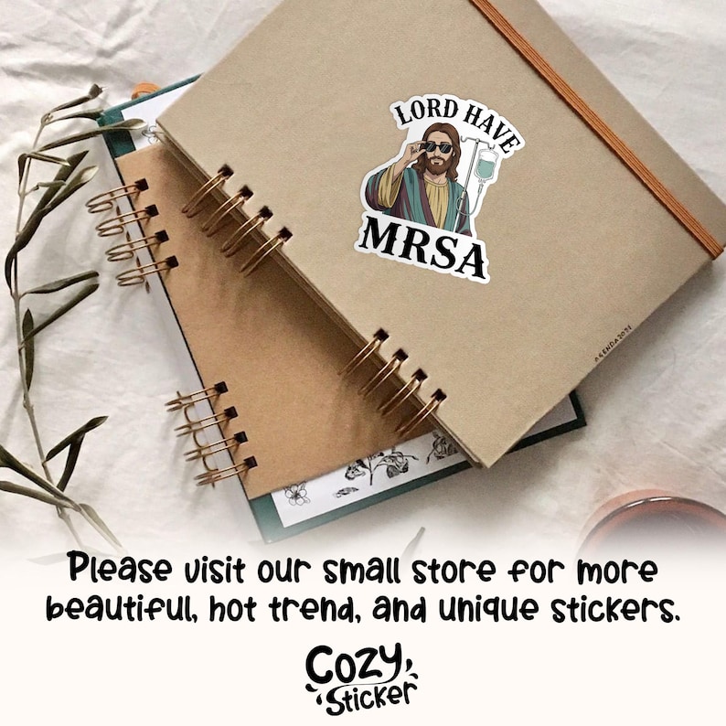 May include: A sticker featuring an illustration of Jesus wearing sunglasses and an IV drip, with the text "LORD HAVE MRSA." The sticker is placed on a brown notebook. The image also includes the text "Please visit our small store for more beautiful, hot trend, and unique stickers."
