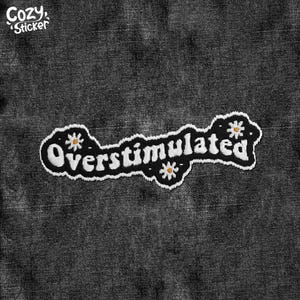 May include: A black and white embroidered patch with the word "Overstimulated" in a whimsical font, adorned with small daisy accents. The patch is set against a dark denim background, with the "Cozy Sticker" logo in the upper left corner.