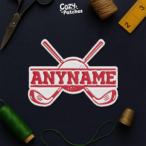 May include: Embroidered patch with a golf theme. The patch features the word "ANYNAME" in red, with a golf ball and crossed golf clubs design. The patch is white with red accents. The patch is surrounded by sewing tools.