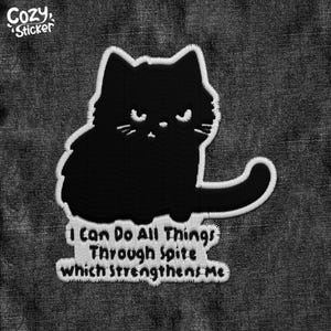 May include: Black and white embroidered iron-on patch featuring a cartoon cat with the text "I can do all things through spite which strengthens me".