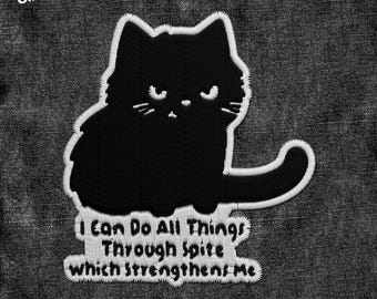 May include: Black and white embroidered iron-on patch featuring a cartoon cat with the text "I can do all things through spite which strengthens me".