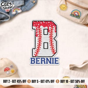 May include: Embroidered patch featuring a baseball-themed letter "B" in white with red stitching and a red top. The name "BERNIE" is embroidered in blue below the letter. The patch is surrounded by other patches and accessories.