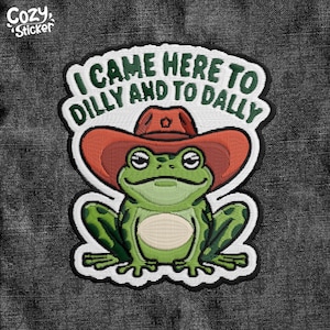 May include: Embroidered patch featuring a green frog wearing a red cowboy hat. The patch has the text "I CAME HERE TO DILLY AND TO DALLY" in green. The patch is on a dark gray denim background. The brand name "Cozy Sticker" is in the top left corner.