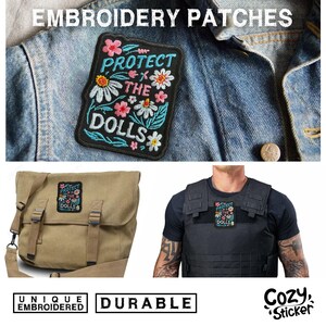 May include: Embroidered patch with the text "PROTECT THE DOLLS" surrounded by colorful flowers and leaves. The patch is displayed on a denim jacket, a messenger bag, and a tactical vest. The patch is described as unique and durable.