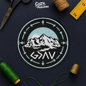 Peut inclure: Écusson rond noir avec un motif de montagne blanc et bleu clair. Le patch comporte le texte "G>AV" et les mots "Cozy Patches". Il est entouré d'une bordure bleu clair avec des flèches.