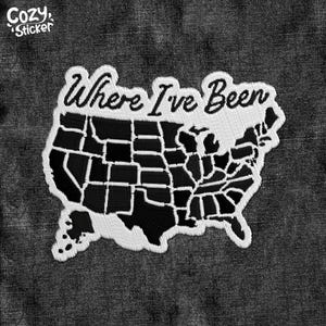 May include: A black and white embroidered patch in the shape of the United States, with the words "Where I've Been" in cursive. The patch is on a dark gray denim background. The Cozy Sticker logo is in the upper left corner.
