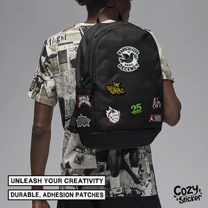 May include: Black backpack with multiple colorful patches. Patches include text and graphics such as a basketball, a bird, and the number 25. The backpack has a side pocket and a top handle. Text on the image reads: "UNLEASH YOUR CREATIVITY" and "DURABLE, ADHESION PATCHES."