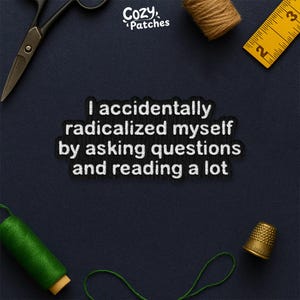 May include: A black patch with white text: "I accidentally radicalized myself by asking questions and reading a lot." Sewing tools surround the patch, including scissors, thread, and a thimble. A yellow tape measure is also present.
