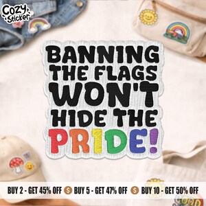 May include: A white sticker with the text "BANNING THE FLAGS WON'T HIDE THE PRIDE!" in black and rainbow colours. The sticker has a decorative border. Other items are visible in the background.