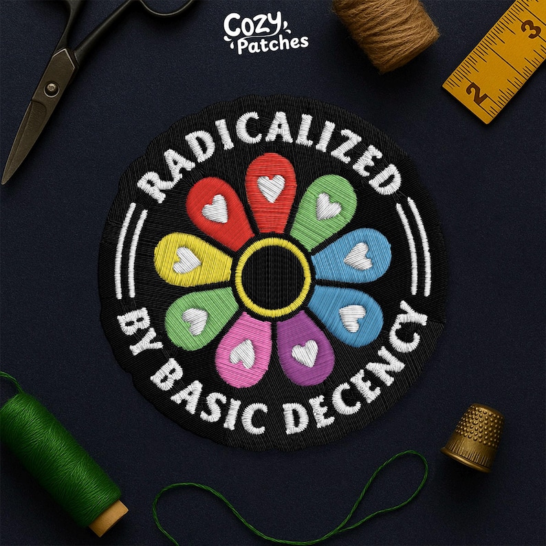 May include: Embroidered patch with a black background and a colorful flower design. The flower petals are in various colors, each with a white heart. The text "RADICALIZED BY BASIC DECENCY" is embroidered in white.
