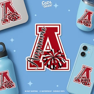 May include: A custom vinyl sticker featuring a large red block letter A with a white outline. The letter is decorated with a black, white, and red cheerleader pom-pom graphic. The word Anyname is written in a black cursive script across the letter.