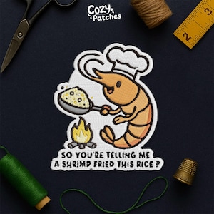 May include: Embroidered patch featuring a cartoon shrimp wearing a chef's hat, holding a pan of fried rice over a small fire. The text reads, "SO YOU'RE TELLING ME A SHRIMP FRIED THIS RICE ?" The patch is from Cozy Patches.