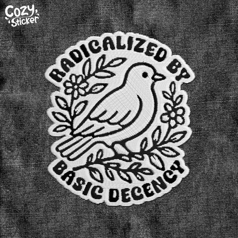 May include: Embroidered patch with a white bird design, surrounded by leaves and flowers, and the text "RADICALIZED BY BASIC DECENCY". The patch is on a dark grey denim background. The words "Cozy Sticker" are in the upper left corner.