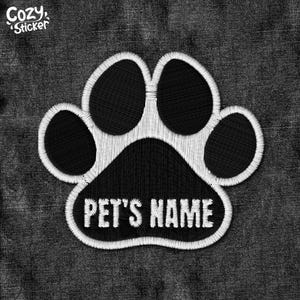 May include: White paw print with black interior and the text "PET'S NAME" in the center, on a dark denim background.