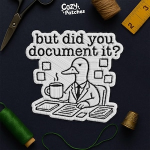 May include: Embroidered patch featuring a duck in a suit holding a coffee mug, with the text "but did you document it?". The patch is white with black outlines and details. The Cozy Patches logo is in the upper left corner.