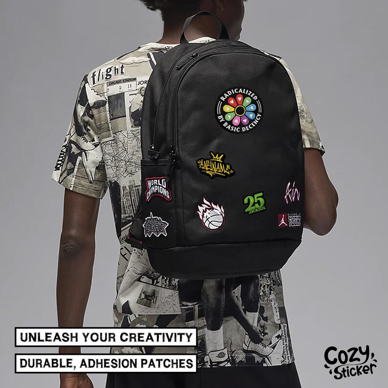 May include: Black backpack adorned with colorful patches, including text that reads "RADICALIZED BY BASIC DECENCY" and "25". The backpack also features patches with basketball and crown designs. The text "UNLEASH YOUR CREATIVITY" and "DURABLE, ADHESION PATCHES" are also visible.