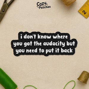 May include: A black embroidered patch with white text that reads "i don't know where you got the audacity but you need to put it back." The patch is surrounded by sewing supplies, including scissors, thread, and a measuring tape.