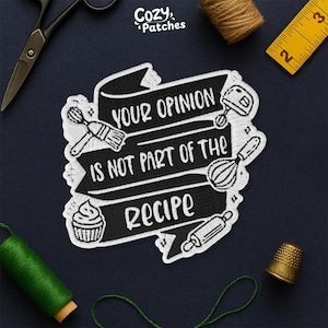 May include: Black and white embroidered patch with the text "YOUR OPINION IS NOT PART OF THE RECIPE". The patch features illustrations of baking tools like a whisk, mixer, and rolling pin. The patch is surrounded by other sewing tools.