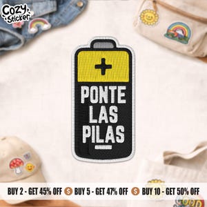 May include: A black and yellow battery-shaped patch with the text "PONTE LAS PILAS" in white. The patch has a white border and a plus sign on the yellow top. The patch is surrounded by other patches and accessories.