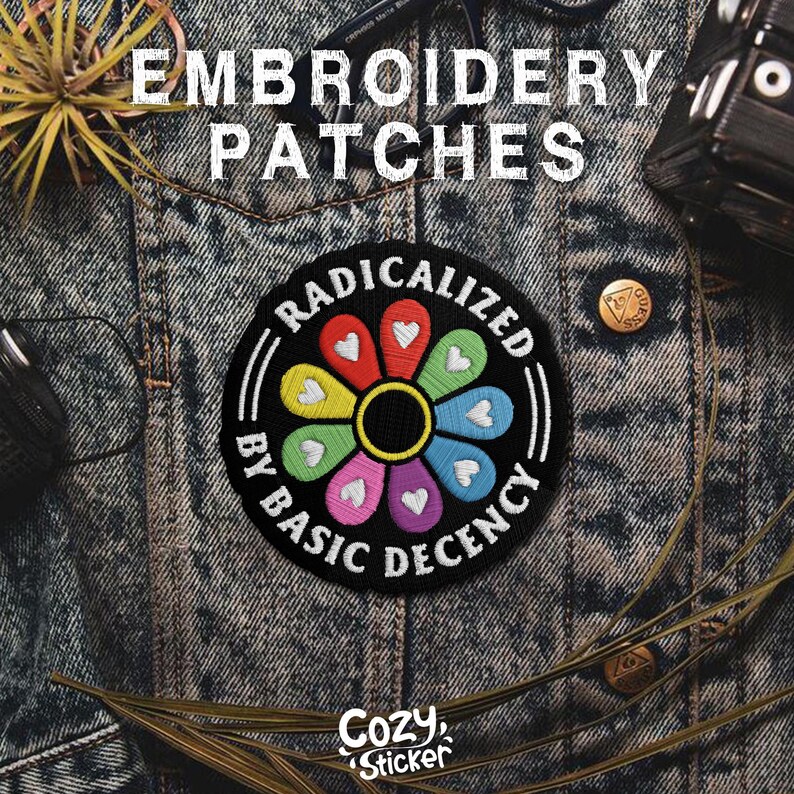 May include: Embroidered patch with the text "RADICALIZED BY BASIC DECENCY" in a circular design. The patch features a colorful flower with heart-shaped petals. The patch is on a denim jacket.