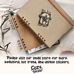 May include: Two spiral-bound notebooks with a sticker that reads "Dost Thou Even Froist?" featuring a weightlifting knight. The notebooks are tan and brown, with a green and white floral design peeking out from underneath.
