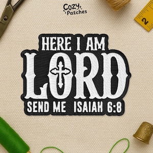 May include: Embroidered patch with the text "HERE I AM LORD SEND ME ISAIAH 6:8" in white on a black background. The patch features a cross design and is surrounded by a black border. The patch is on a beige fabric.