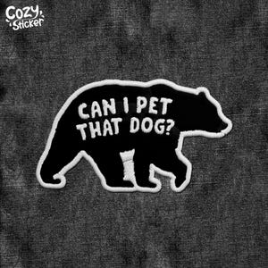May include: Black felt patch with white stitching in the shape of a bear. The bear is walking and has the text "Can I pet that dog?" written on its back.