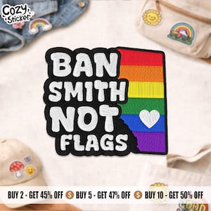 Peut inclure: Écusson brodé avec le texte "BAN SMITH NOT FLAGS" en blanc sur fond noir. Le côté droit présente un drapeau arc-en-ciel avec un cœur blanc. L'écusson est entouré d'autres accessoires.
