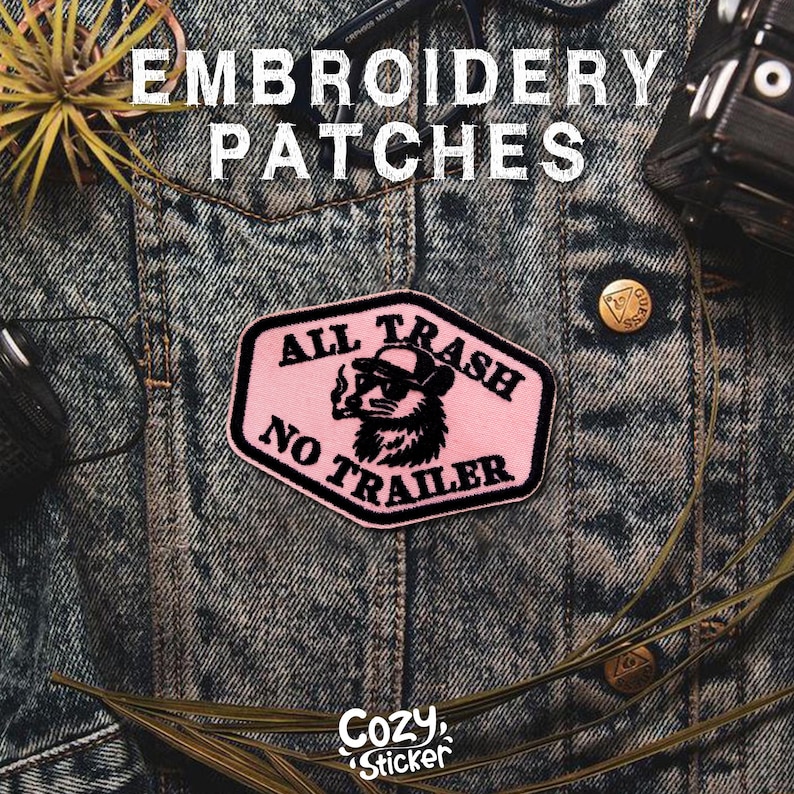May include: Pink embroidered patch with the text "ALL TRASH NO TRAILER" and a raccoon wearing sunglasses and a hat, smoking a cigarette. The patch is on a denim jacket. The words "Embroidery Patches" are at the top.
