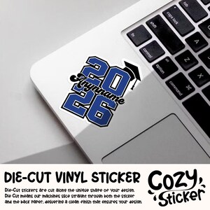 May include: A die-cut vinyl sticker with the text "2026" in blue with a white outline, a graduation cap, and a personalized name. The sticker is on a laptop.
