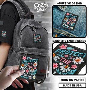 May include: Embroidered patch with the text "PROTECT THE DOLLS" surrounded by pink and white flowers. The patch is shown on a backpack and a denim jacket. The patch is an adhesive design and iron-on.