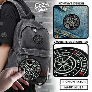 May include: Black embroidered patch with a compass design and the text "NOT ALL THOSE WHO WANDER ARE LOST." The patch is round and has a red border. The image also shows the patch on a backpack and denim jacket.